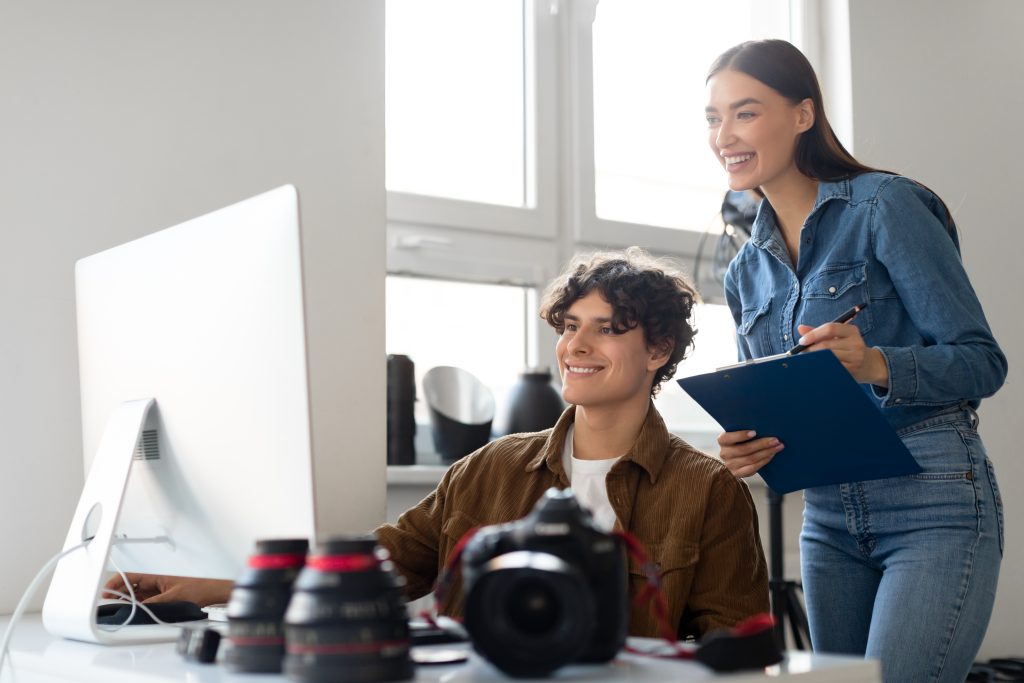 happy professional team of photographer and assistant looking at computer monitor, transfering and selecting photos