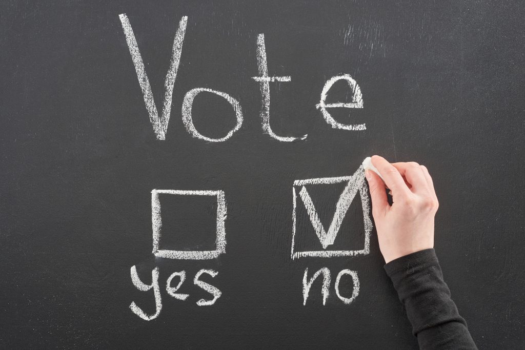 top view of voter putting check mark near no word on black chalkboard